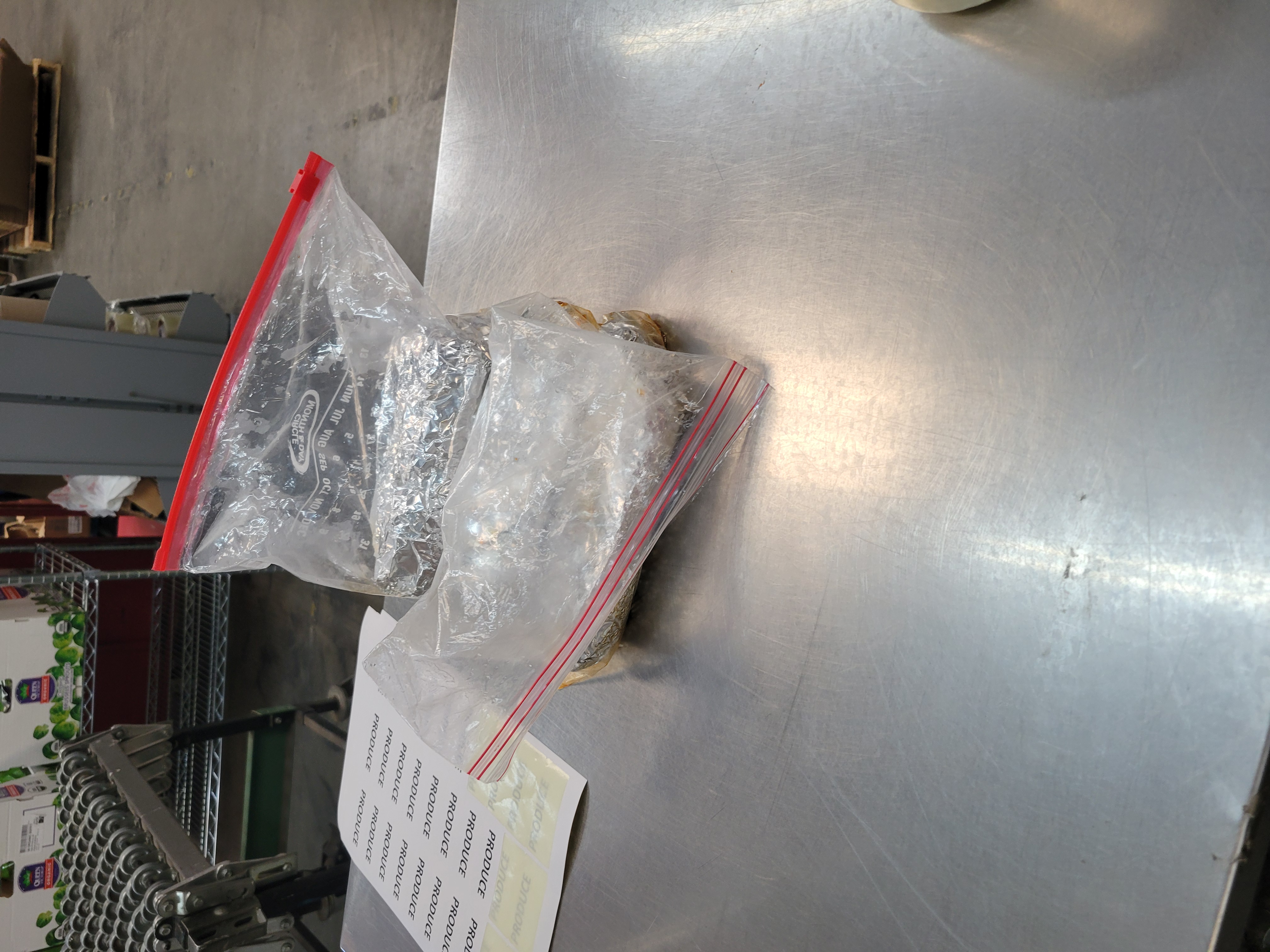 Two zip lock gallon bags filled with burritos next to dry goods labels on metal table.